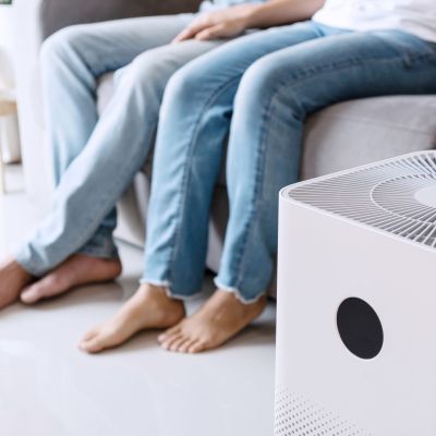 Close up of white air purifier on the floor in living room the background of young Asian couple relaxes on sofa. Concept of caring for fresh air at home. Caring for well-being and health.